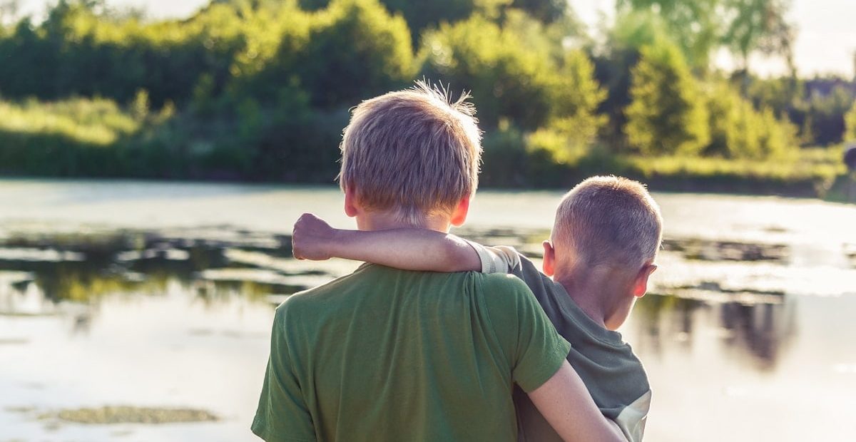 two brothers toghere are standing in front of a pond